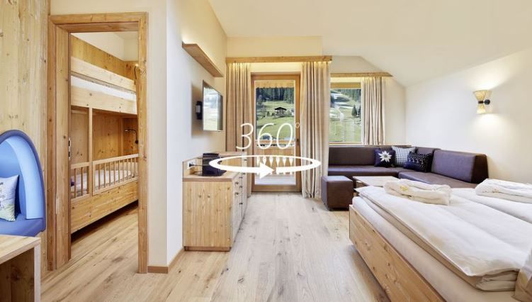 Helles Wohnzimmer mit Bett, Couch, Balkonzugang, links eine offene Tür mit Stockbett, mittig ein 360° Zeichen.