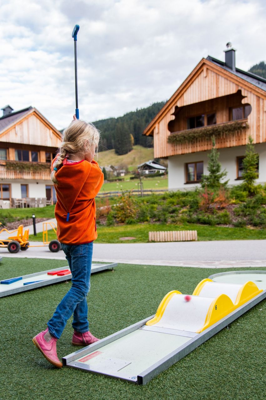 Ein junges Mädchen spielt Minigolf und schwingt dabei mit ihrem Schläger durch die Luft. 