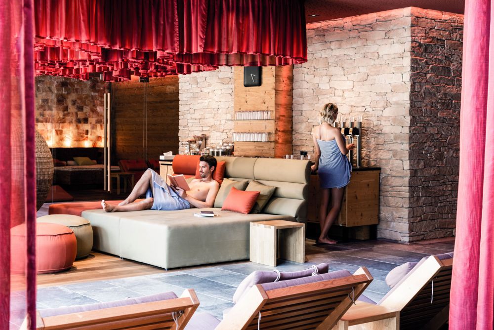 Ein Mann liegt auf einer großen Liege im Wellnessbereich und liest, eine Frau steht dahinter.