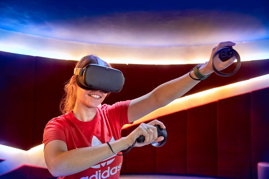 A woman wearing VR goggles, playing and smiling in a virtual reality room.